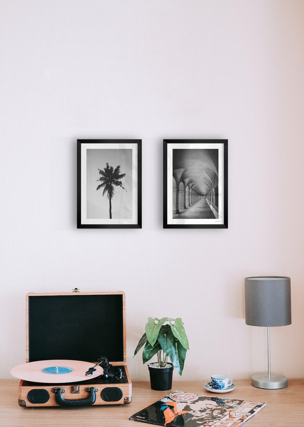 Tavelvägg med ramar i svart i storlekar 21x30 med posters med "Palm" och "Gång med pelare och valv"