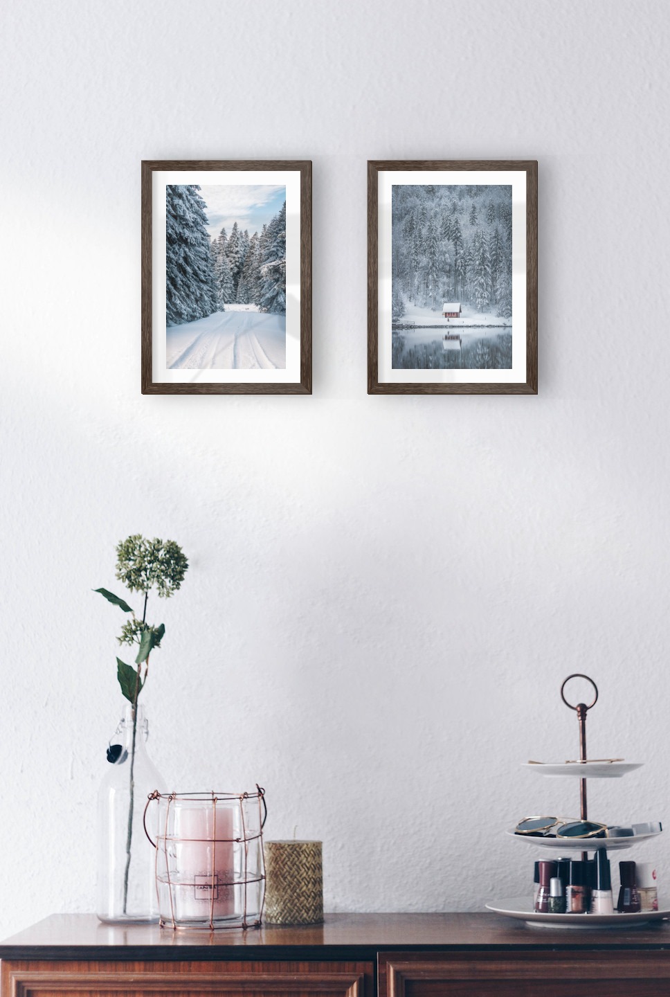 Tavelvägg med ramar i mörkt trä i storlekar 21x30 med posters med "Snöig väg" och "Stuga vid sjö"